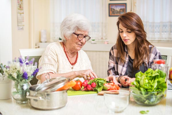 elderly woman and caregiver preparing food together at kitchen.